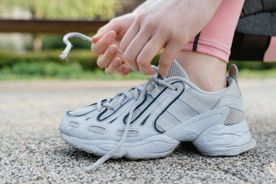Preparing for the marathon journey, a runner ties his shoelaces beside a scenic riverside path, symbolizing determination and readiness. A bottle of water sits close, underscoring the importance of hydration.